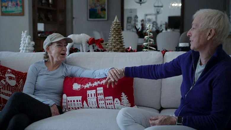 Chris Evert and Martina Navratilova sitting side by side on a couch, their hands clasped, looking at each other with quiet intensity.