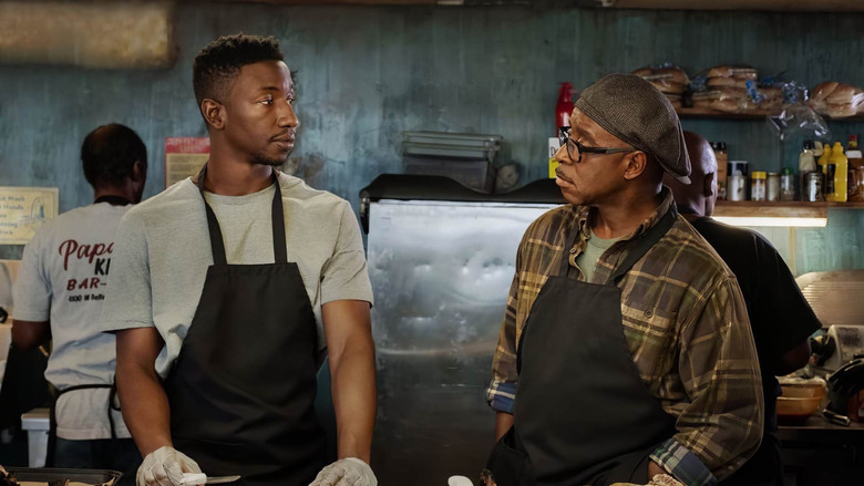 A dimly lit barbecue joint, smoke curling from a grill, with Elijah and Louis standing on opposite sides of the counter, their faces half-lit by the glow of the coals.