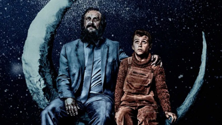 A dimly lit room where a father and son sit together, the glow of a television casting shadows on their faces
