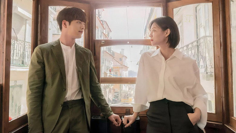 A dimly lit room where Joon-young and Young-jae sit on opposite sides of a table, their expressions a mix of frustration and reluctant curiosity.