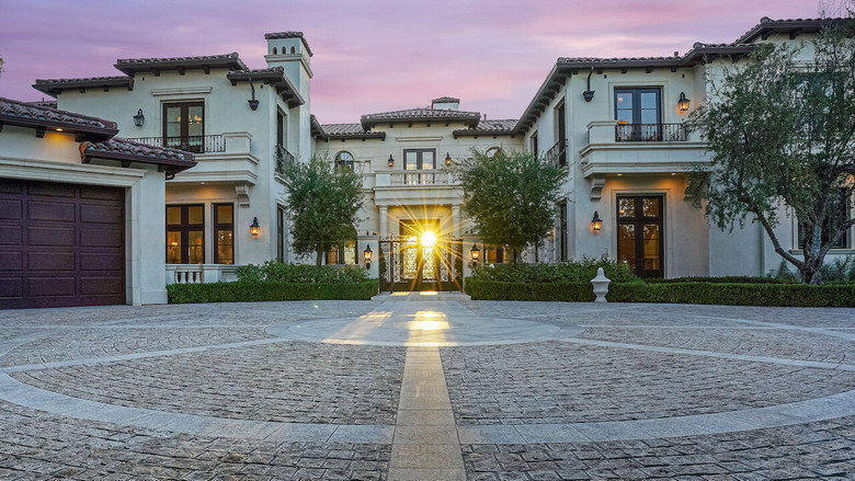 A sunlit Beverly Hills mansion with a sprawling lawn, its white facade gleaming under a cloudless sky