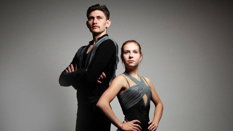A pair of figure skaters mid-routine, their bodies arched in unison against a blurred ice rink backdrop