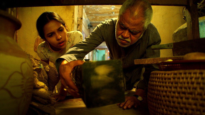 A dimly lit room where a man in a kurta stands over a prone figure, his shadow stretching long across the floor.
