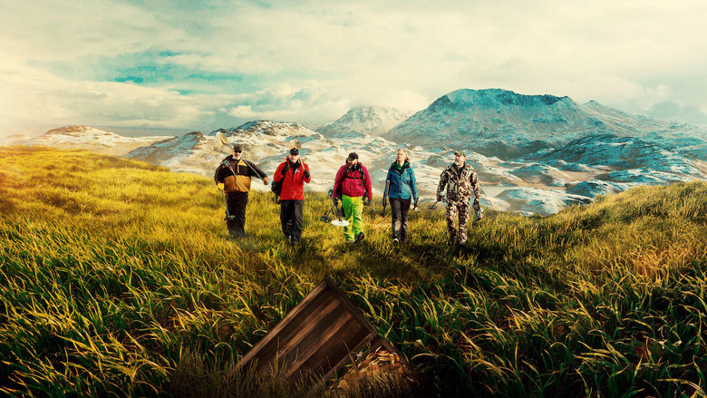 A team of treasure hunters trudges through Adak Island's foggy, windswept landscape, their gear glinting in the dim light.