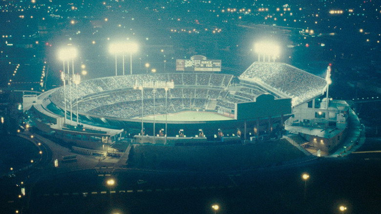 Billy Beane and Peter Brand sit in the empty stands of a baseball stadium, the late afternoon light casting long shadows across the field.