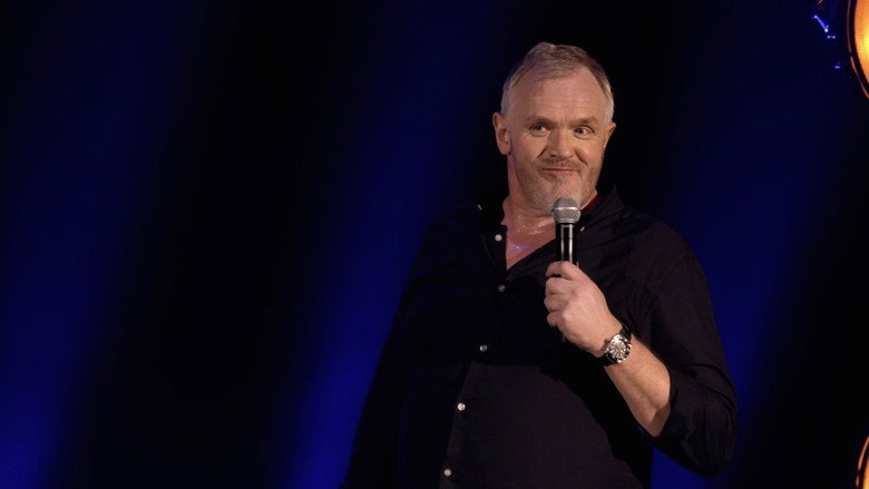 Greg Davies on stage, mid-gesture, his towering frame hunched slightly as if sharing a secret with the audience