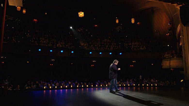 Patton Oswalt on stage, mid-gesture, his face lit with the kind of exhausted intensity that suggests he’s just said something he can’t take back