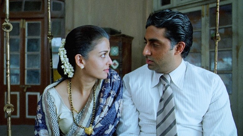A dimly lit room where Gurukant Desai, played by Abhishek Bachchan, stands surrounded by his associates, his expression a mix of determination and fatigue.