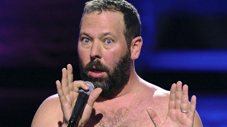 Bert Kreischer on stage, shirtless, arms outstretched, mid-laugh