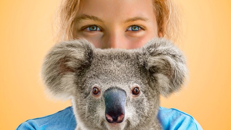 Izzy Bee cradles a young koala, its tiny paws clutching her shirt as sunlight filters through the trees