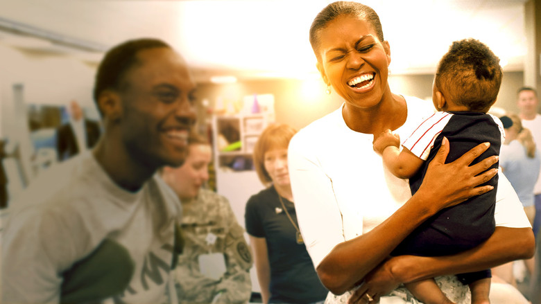 Michelle Obama on stage, bathed in warm light, addressing a packed arena