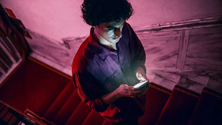 A neon-drenched hotel lobby, where the film’s protagonist Niccolò stands isolated amid the artificial glow, his reflection fractured in the glass.