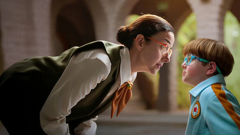 A close-up of Dora’s hands as she adjusts a name tag on a student’s uniform, her fingers trembling slightly—whether from anger or ambition, it’s unclear.