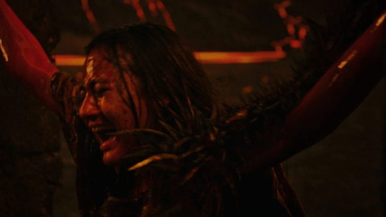 A shadowy figure looms over a bound victim, their face contorted in agony as flames lick at their skin