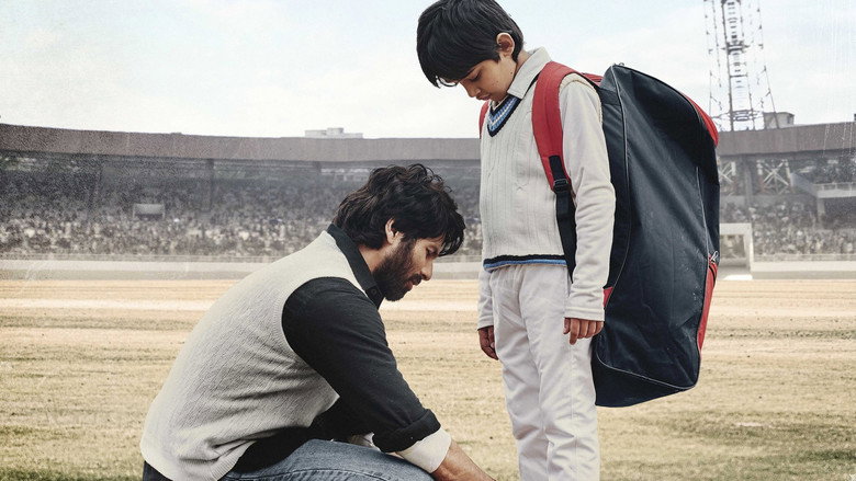 A father and son sit on a rooftop at dusk, the city sprawling behind them, the boy holding a cricket ball while the father stares into the distance.