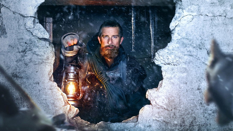 Bear Grylls kneels in the snow, examining a makeshift tool, his breath visible in the frigid air
