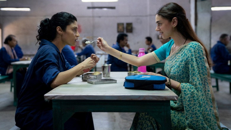 A dimly lit room where two women sit on opposite ends of a couch, their faces half in shadow, the tension between them palpable.