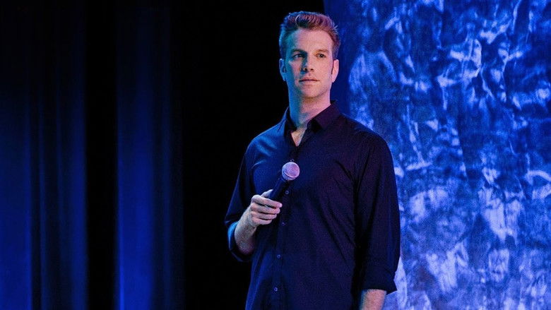 Jeselnik stands alone on a stark stage, bathed in cold light, his expression unreadable as he delivers a punchline that hangs in the air like a threat.