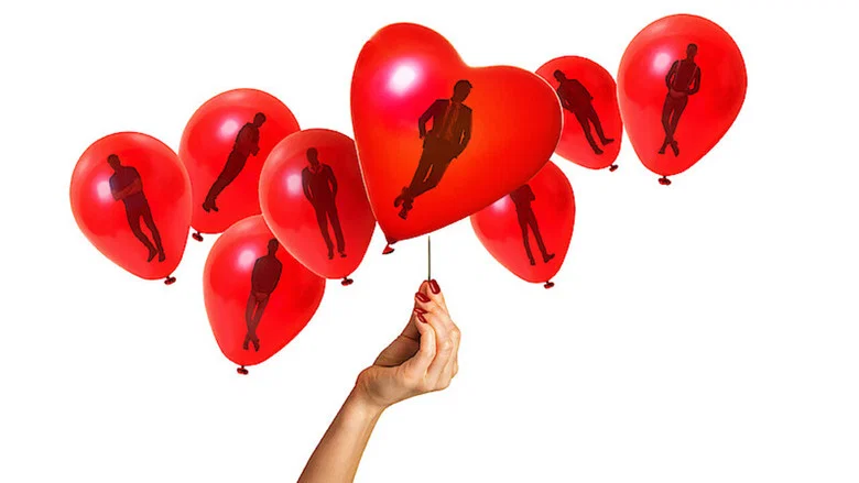 A brightly lit studio set with contestants holding red balloons, their expressions a mix of anticipation and discomfort