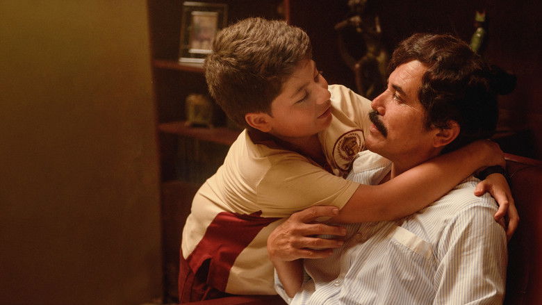 A man standing in a sunlit hallway, looking out a window with a weary, guarded expression.