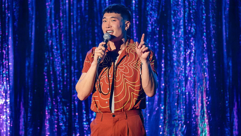 Joel Kim Booster on stage, mid-laugh, arms spread wide as if inviting the audience into a secret