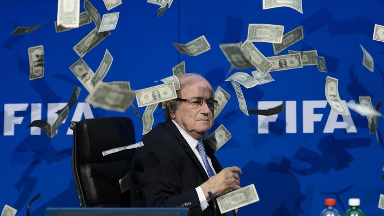 A shadowy figure stands before a wall of FIFA logos, their face obscured by the glare of a spotlight