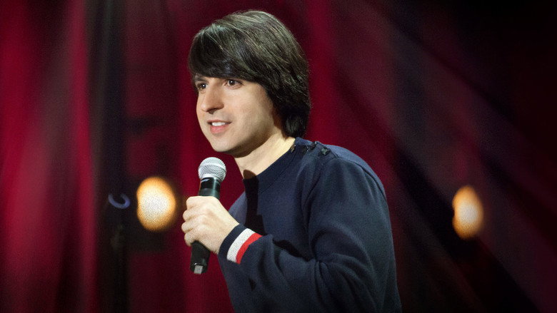 Demetri Martin onstage with a notepad, mid-performance