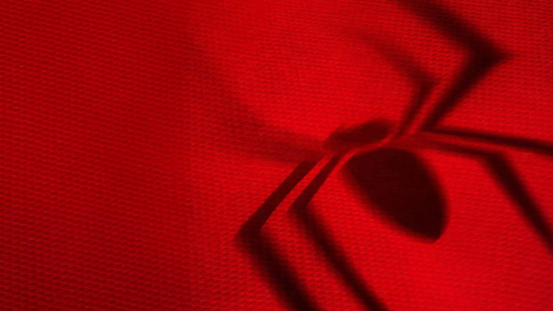 A wide, dimly lit shot of Peter Parker sitting alone in a cluttered New York apartment, the city lights blurring outside his window.