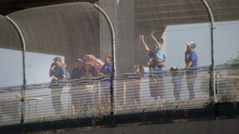 Families rushing toward each other in the dry riverbed, the border wall looming behind them