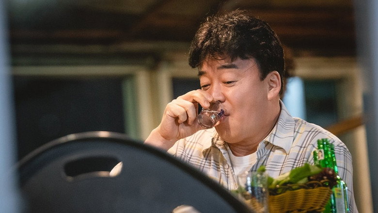 A dimly lit table set with Korean banchan, soju bottles, and two empty glasses, the steam from a hot dish curling into the air