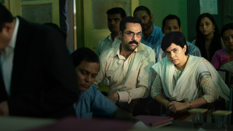 Neelam Krishnamoorthy standing in a dimly lit room, her expression a mix of exhaustion and quiet determination