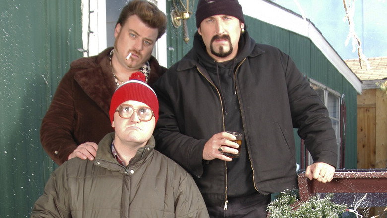 Three men in winter coats stand around a bonfire at night, their faces lit by the flames.