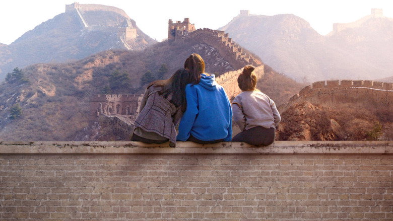 Three teenage girls stand together in a sunlit courtyard, their faces turned toward the camera with expressions that mix curiosity and quiet resolve.