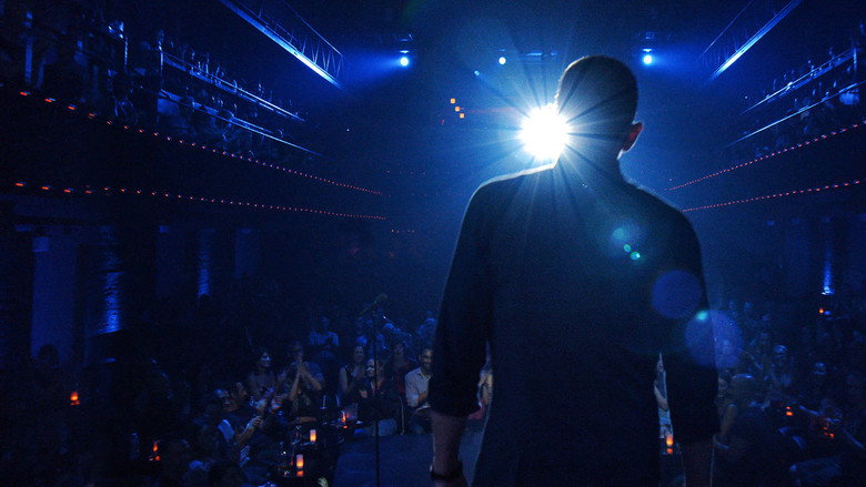 A dimly lit stage with a single spotlight, a microphone stand, and an empty stool, waiting for the next comedian to take the stage.