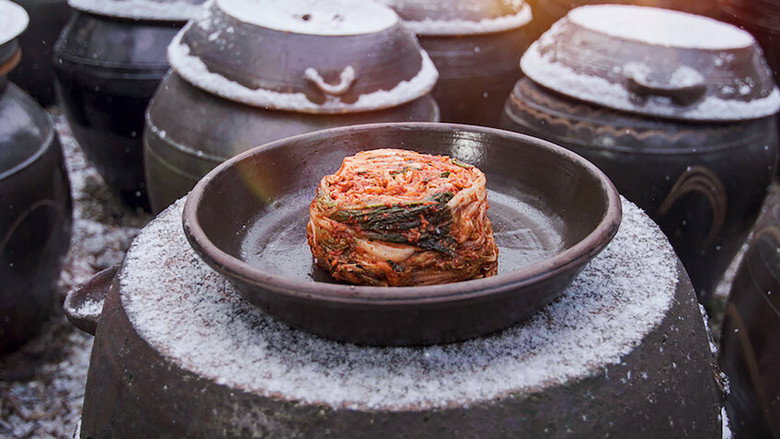A close-up of hands massaging salt into napa cabbage, the leaves glistening under warm light