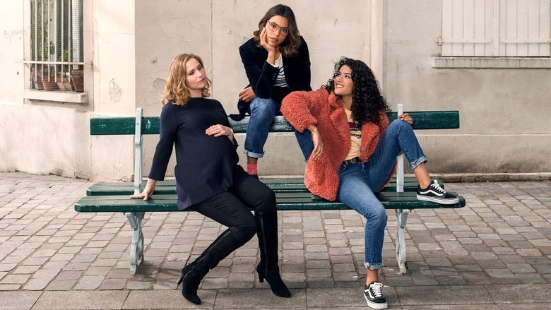 Three friends laughing on a Parisian balcony, the city's rooftops stretching behind them