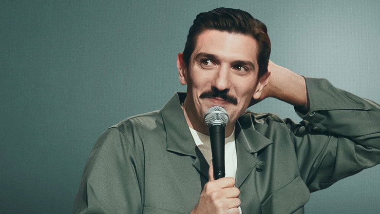 Andrew Schulz on stage at the Beacon Theatre, mid-gesture, bathed in warm light