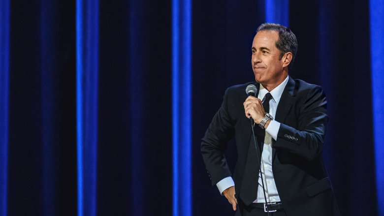Jerry Seinfeld on stage at the Beacon Theatre, mid-gesture, his face lit with the kind of exaggerated disbelief that has become his trademark