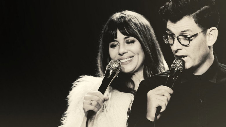 Natasha Leggero and Moshe Kasher on stage, mid-laugh, with a neon-lit backdrop that reads "The Honeymoon Stand Up Special"