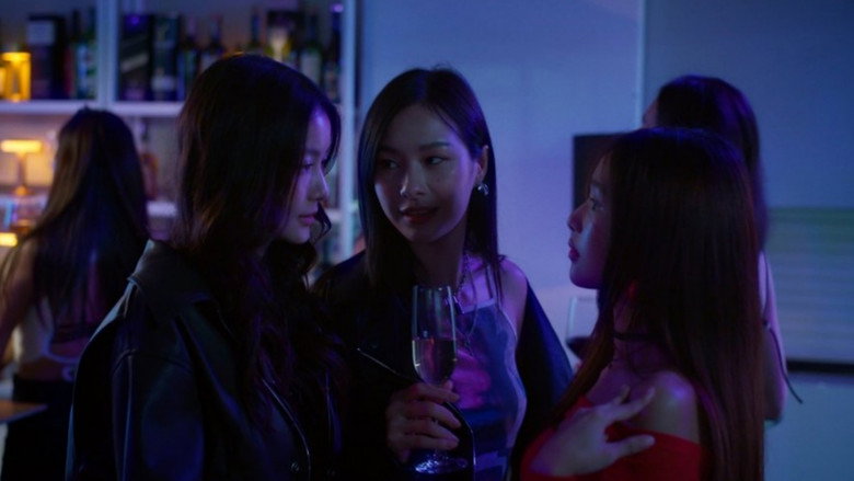 The main cast gathered in a dimly lit, cluttered living room, reflecting the intimacy and tension of their shared history.