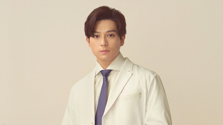 A dimly lit hospital corridor, where Dr. Tokushige stands with his back to the camera, speaking softly to a patient whose face we can’t see. The fluorescent lights hum overhead, casting long shadows that stretch like unanswered questions.