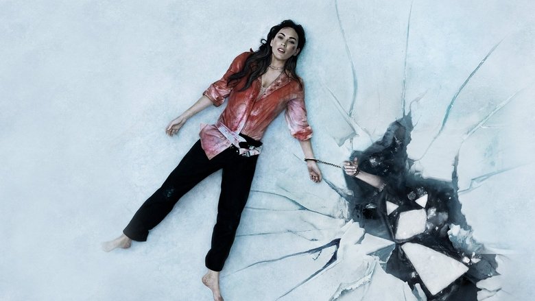 A woman in a bloodstained nightgown stands in a dimly lit room, her wrist chained to a lifeless body on the floor