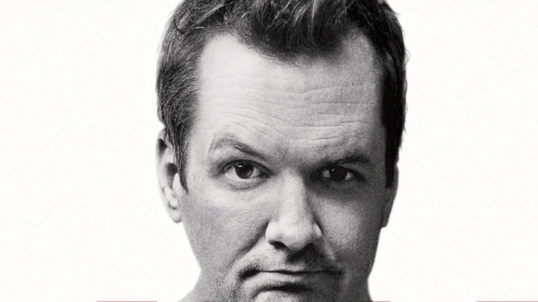 Jim Jefferies on stage, mid-performance, his face lit with the kind of grin that suggests he’s about to say something you’ll regret laughing at.