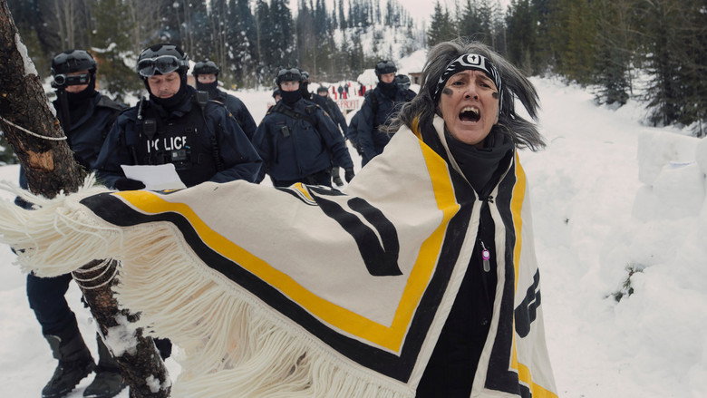 A line of RCMP officers in tactical gear facing off against Wet’suwet’en land defenders in a misty forest