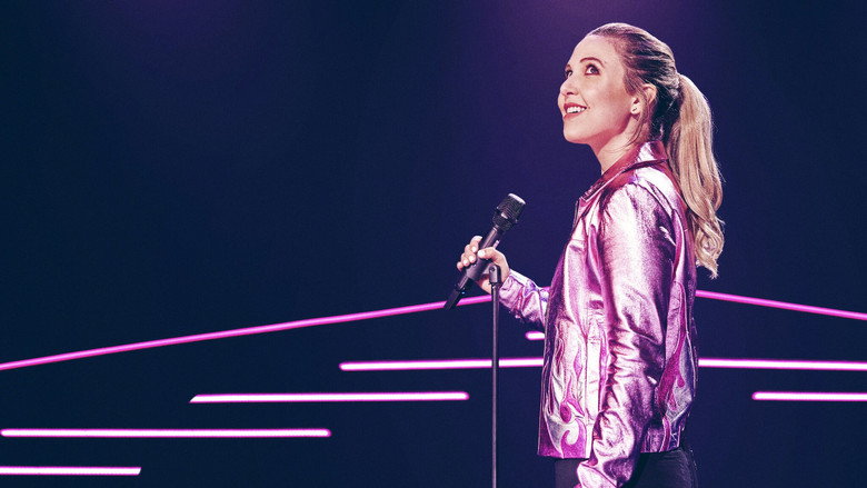 Taylor Tomlinson on stage, bathed in neon light, mid-laugh as she delivers a punchline