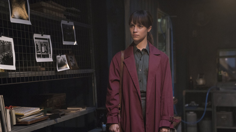 Alicia Vikander as Lucy Fly, standing in a dimly lit Tokyo alley, her face half-hidden in shadow.