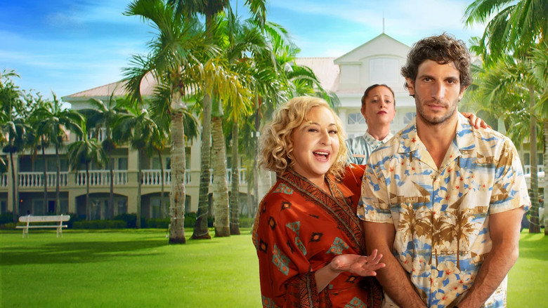 A sunlit balcony overlooking a tropical beach, where a man in a white shirt stares blankly at the horizon while his mother, mid-laugh, gestures animatedly beside him