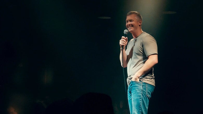 A wide shot of the stage, the crowd barely visible in the dark, McCusker illuminated under a single spotlight