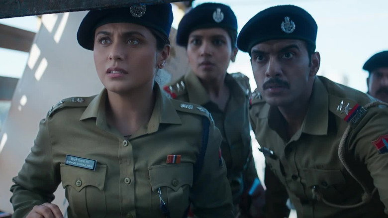 A tense confrontation in a dimly lit room, Shivani Shivaji Roy standing over a suspect with a mix of fury and calculation.