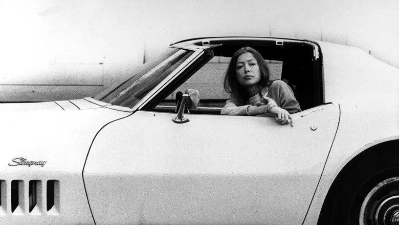 Joan Didion in her New York apartment, bathed in soft light, her hands folded in her lap as she speaks to the camera.